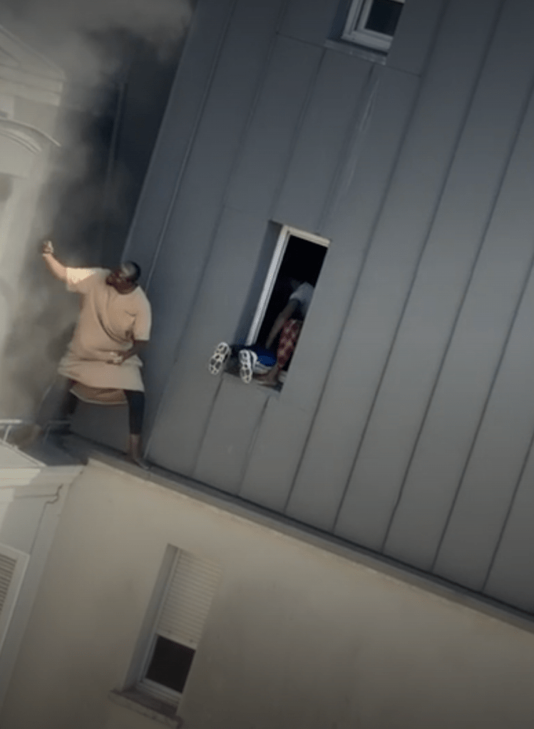 Man climbs along the outside of a building through heavy smoke to reach a child at a window during a fire rescue.
