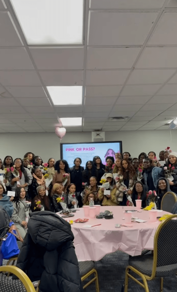 A large group of students gathered in a decorated event space holding flowers and notes during a Hearts of Harmony program focused on women’s wellness and affirmation.