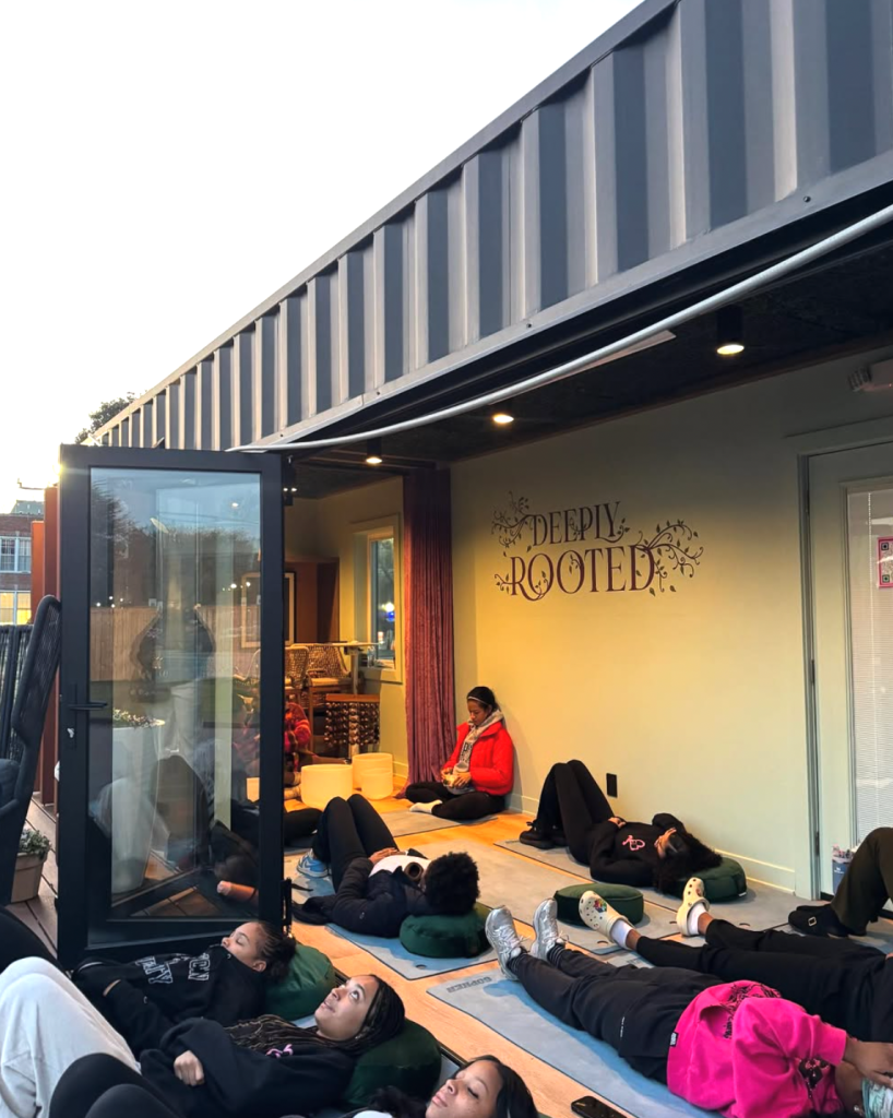 Students participate in a Hearts of Harmony wellness session, lying on mats during a guided sound bath inside the Deeply Rooted studio.