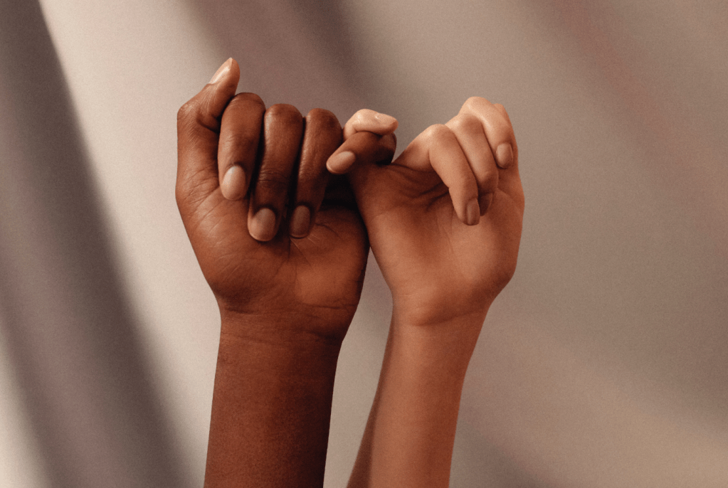 Two African American hands holding each other at the pinky. 