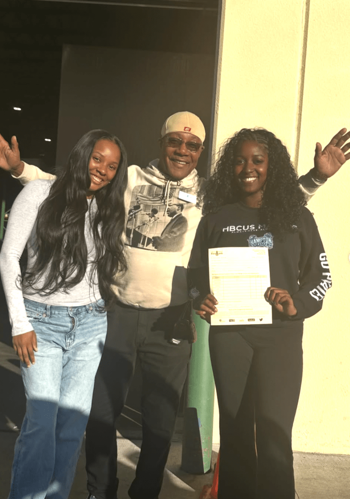 Miracle Gross and volunteer Krystian Sellers, smiling with an employee at the Virginia Peninsula Foodbank while holding the official donation receipt.