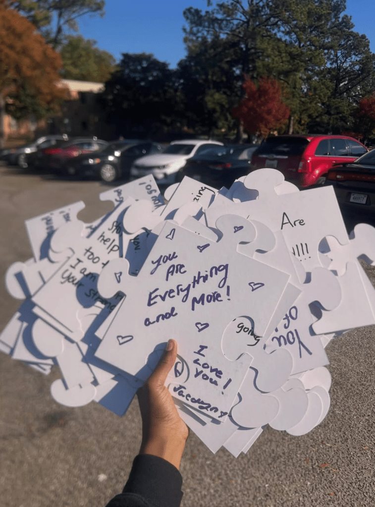 A hand holding multiple white puzzle pieces covered with handwritten encouraging messages for the Puzzles of Peace  domestic violence awareness project.